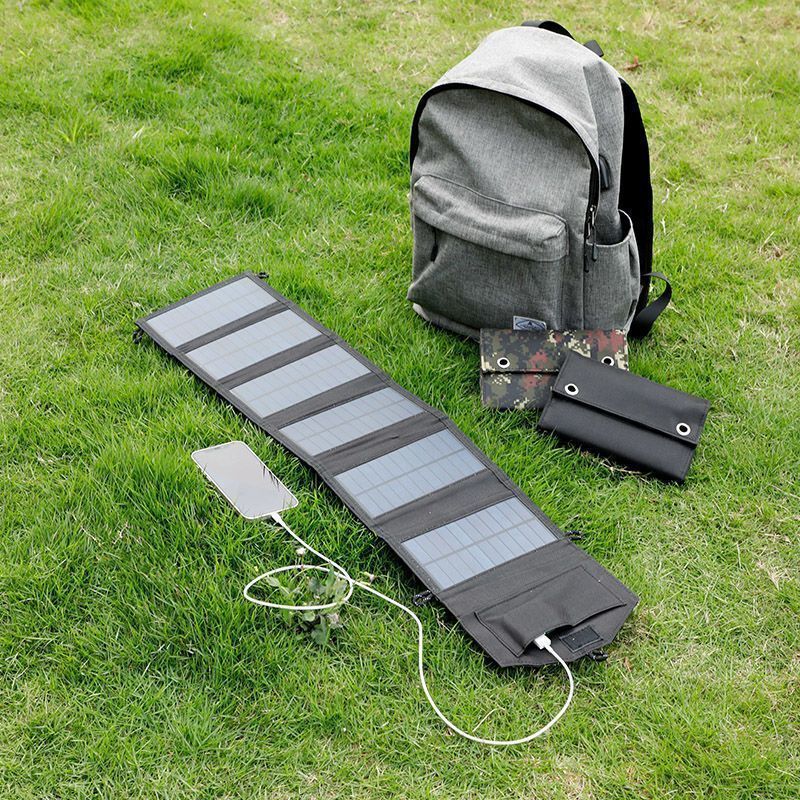 Foldable solar panel with charging cable on grass next to a backpack